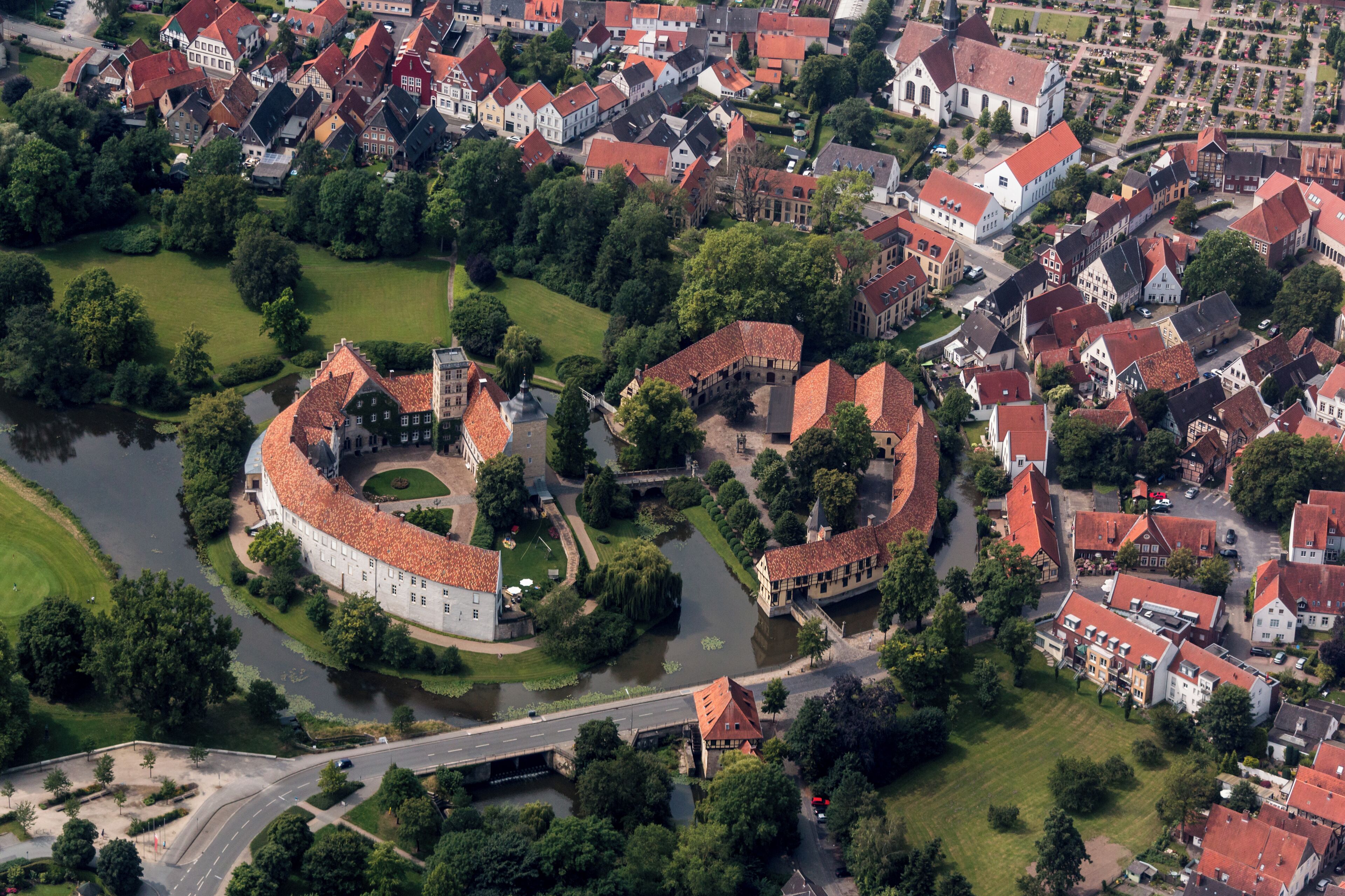 An aerial view of a historic town with a prominent circular fortress, surrounded by traditional buildings and a river.