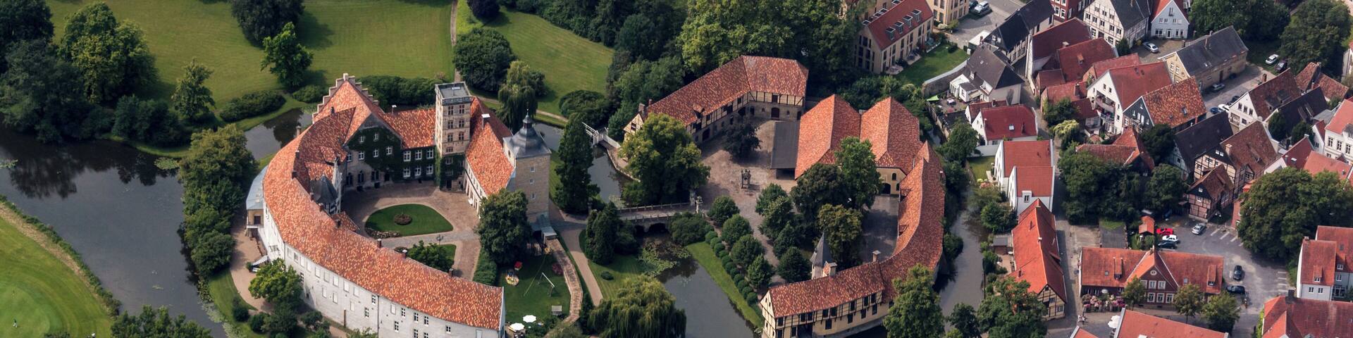 An aerial view of a historic town with a prominent circular fortress, surrounded by traditional buildings and a river.