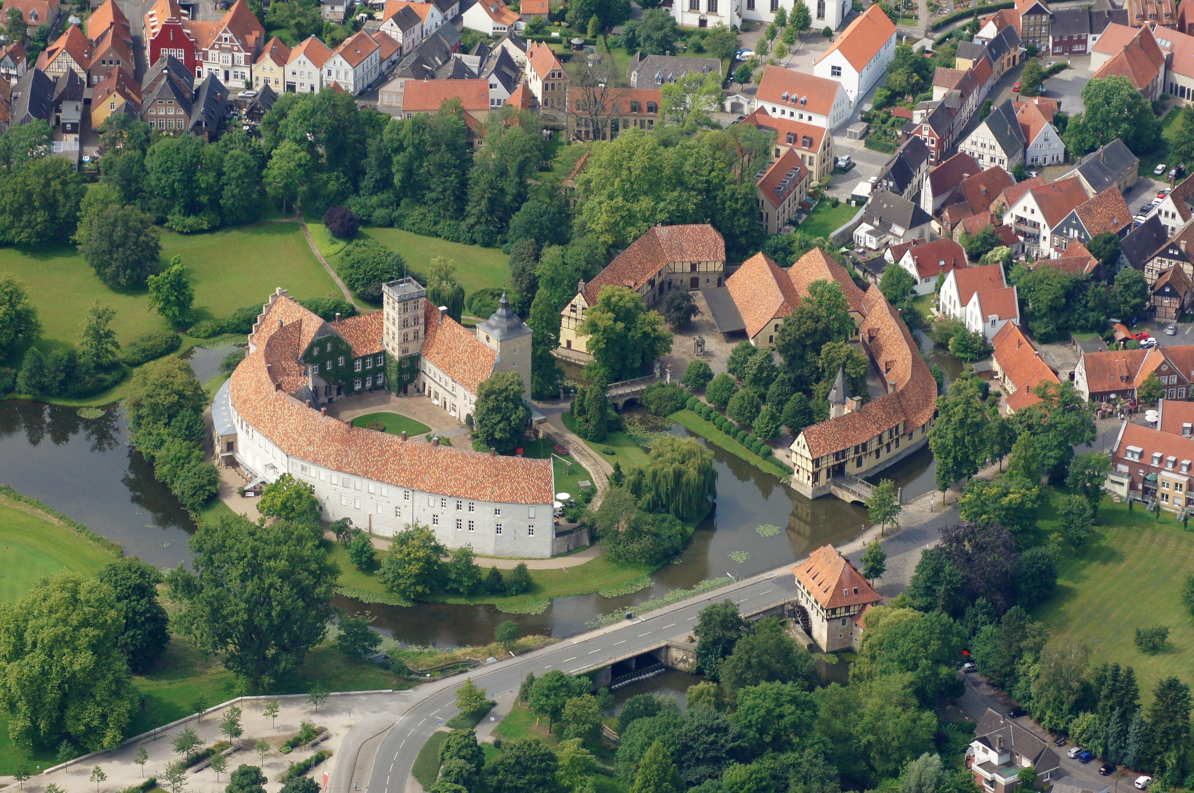 An aerial view of a historic town with a prominent castle, river, and surrounding greenery.