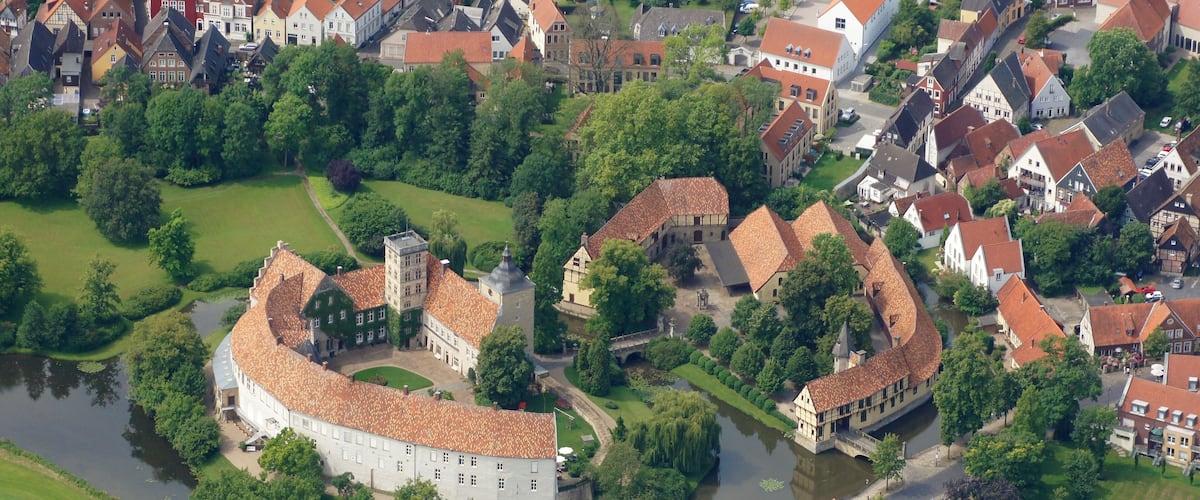 An aerial view of a historic town with a prominent castle, river, and surrounding greenery.