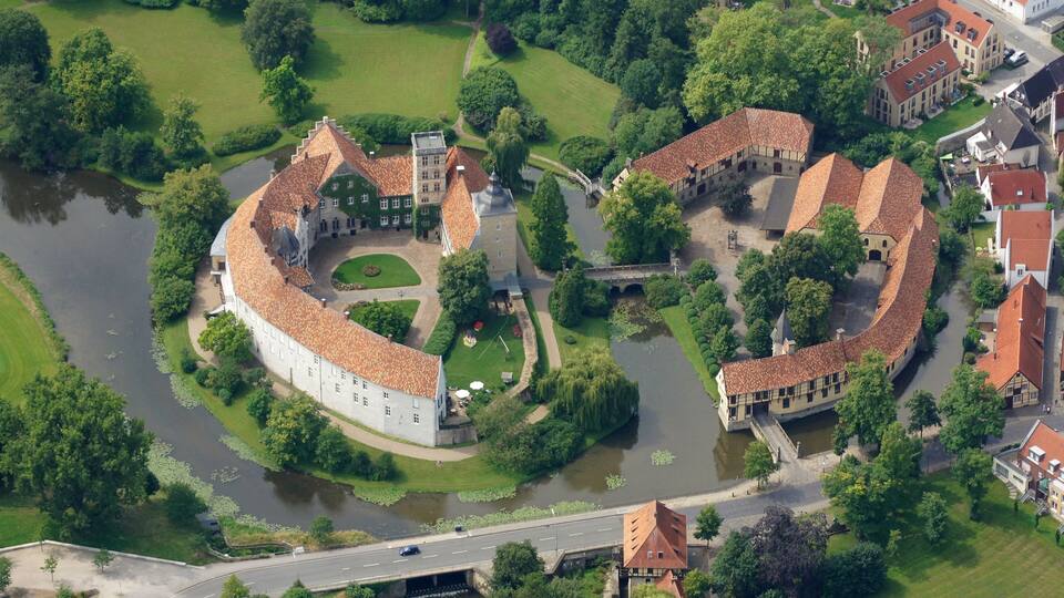 An aerial view of a historic walled town with a river running through it, surrounded by lush greenery and traditional architecture.