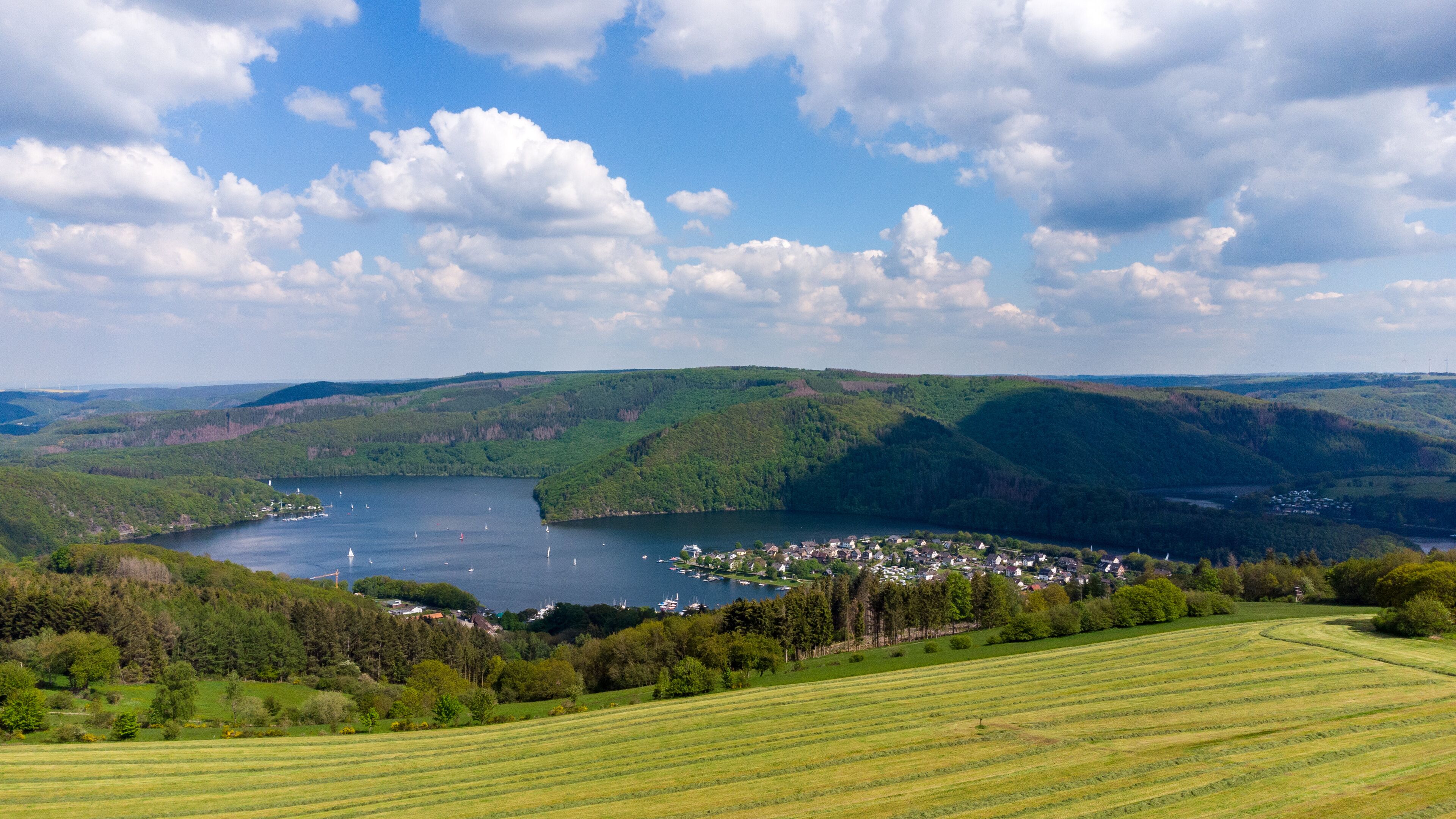 A lake surrounded by green hills, a small town, and sailboats on the water.