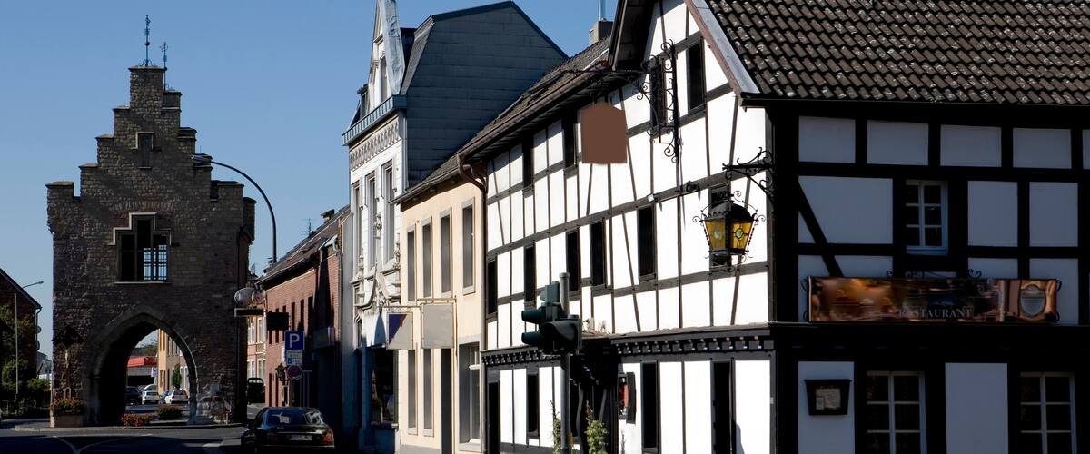 A historic street with a stone archway, traditional half-timbered buildings, and a restaurant sign.