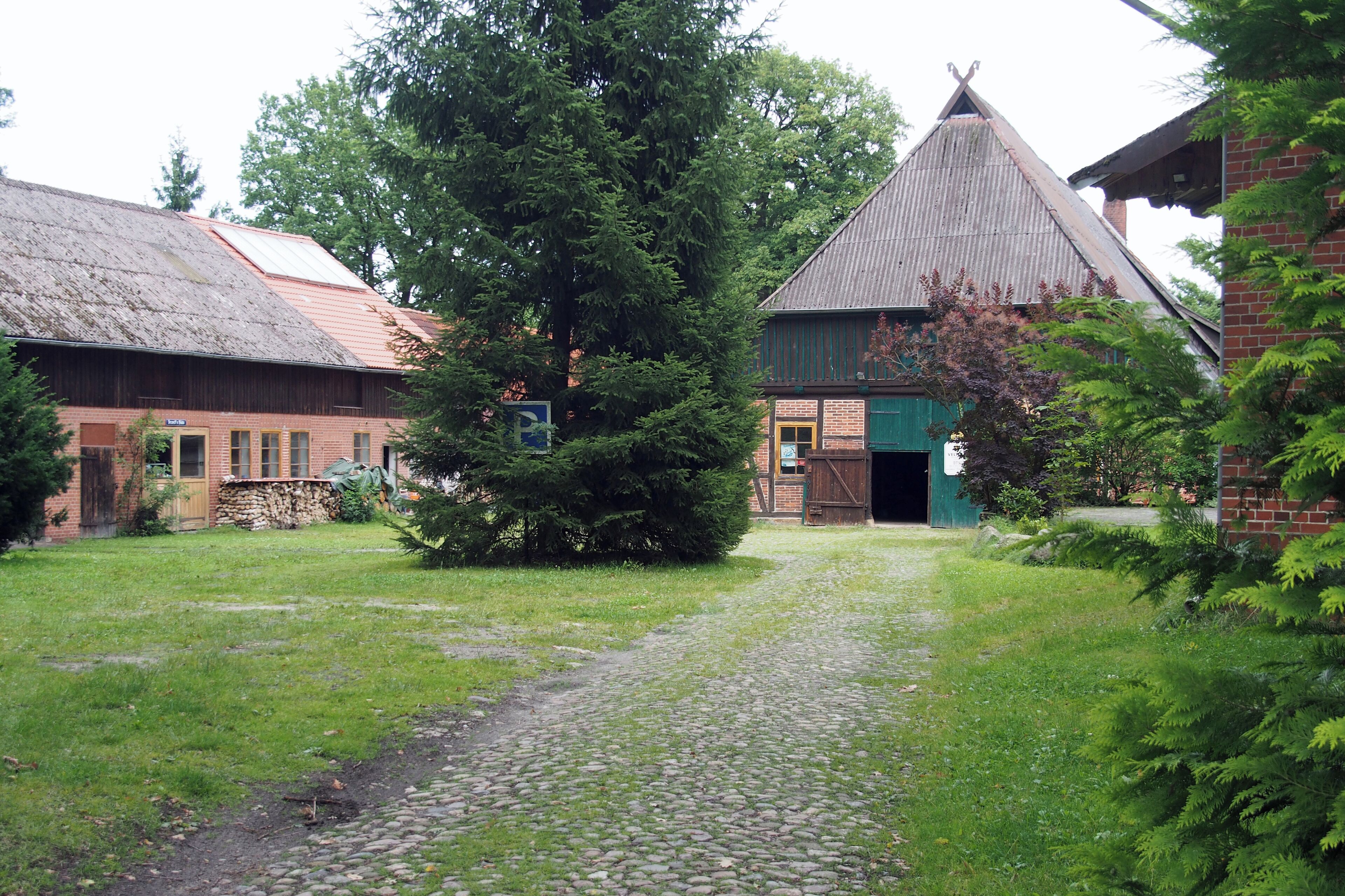 A cobblestone path leading to a rustic building with a green door, surrounded by lush greenery and trees.