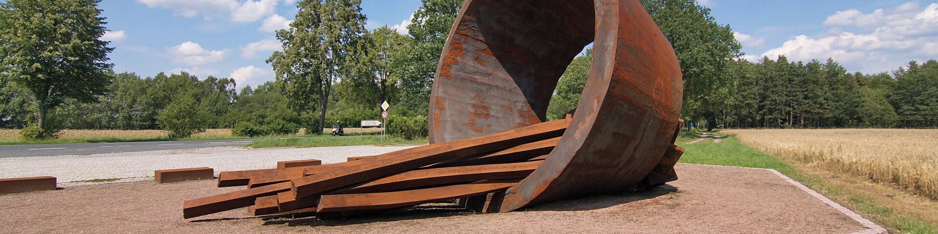 Das Mahnmal soll an die nahe gelegene Bahnrampe erinnern, auf der die Kriegsgefangenen und KZ-Häftlinge ankamen. Sie wurden mit der Reichsbahn hierher transportiert und mussten von hier 5 bis 6 km zu Fuß in das Lager marschieren.
