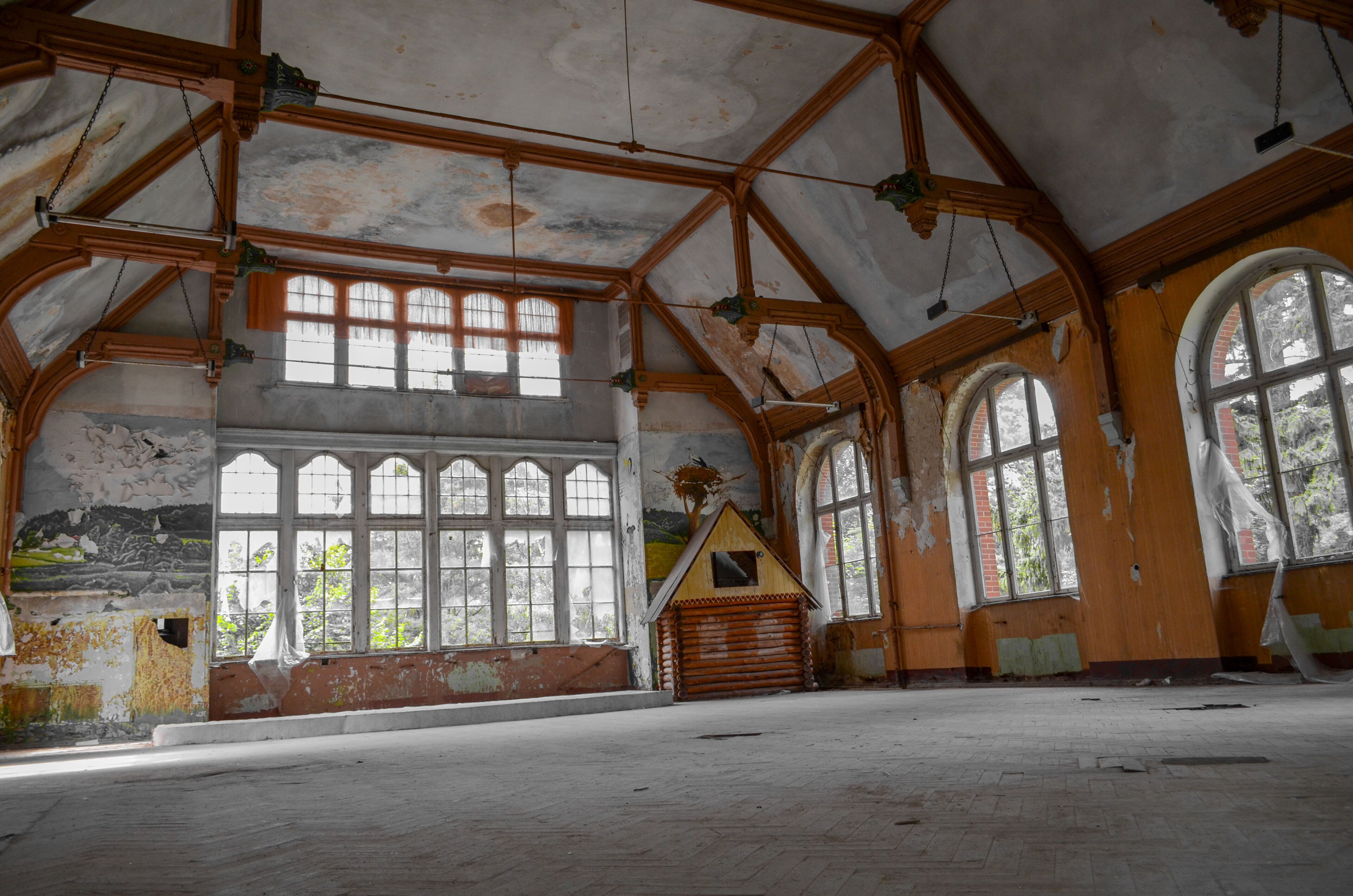 An abandoned building with wooden beams, large arched windows, and a small wooden structure.
