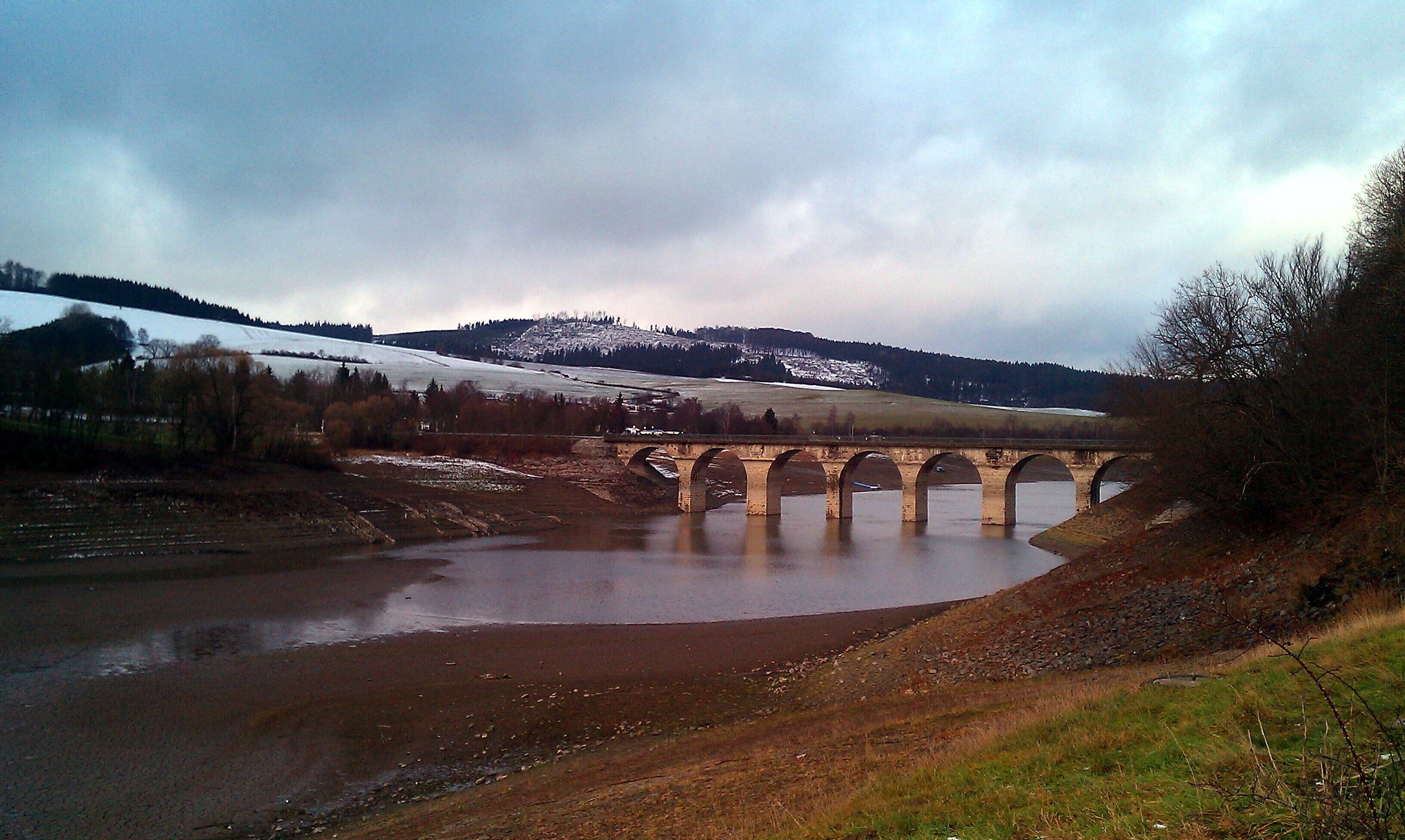 A stone bridge over a river with snow-capped hills in the background.