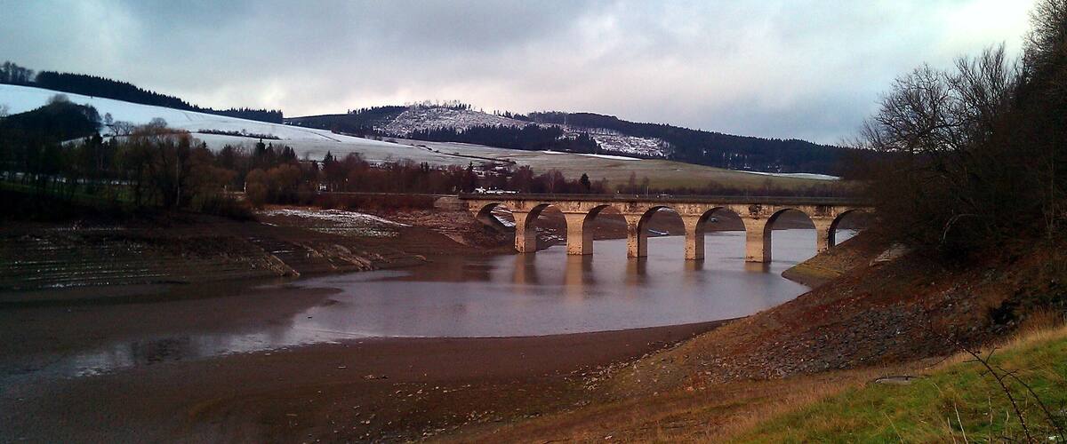 A stone bridge over a river with snow-capped hills in the background.