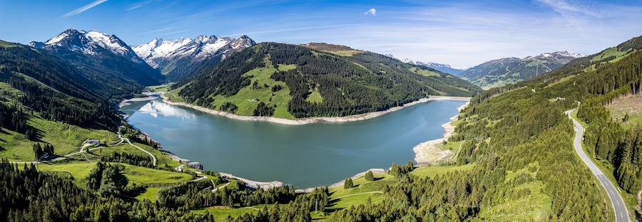 A lake surrounded by mountains, a winding road, and a small building.