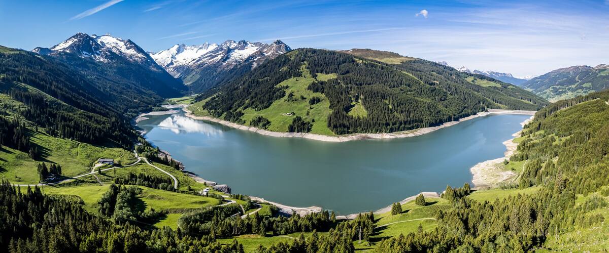 A lake surrounded by mountains, a winding road, and a small building.