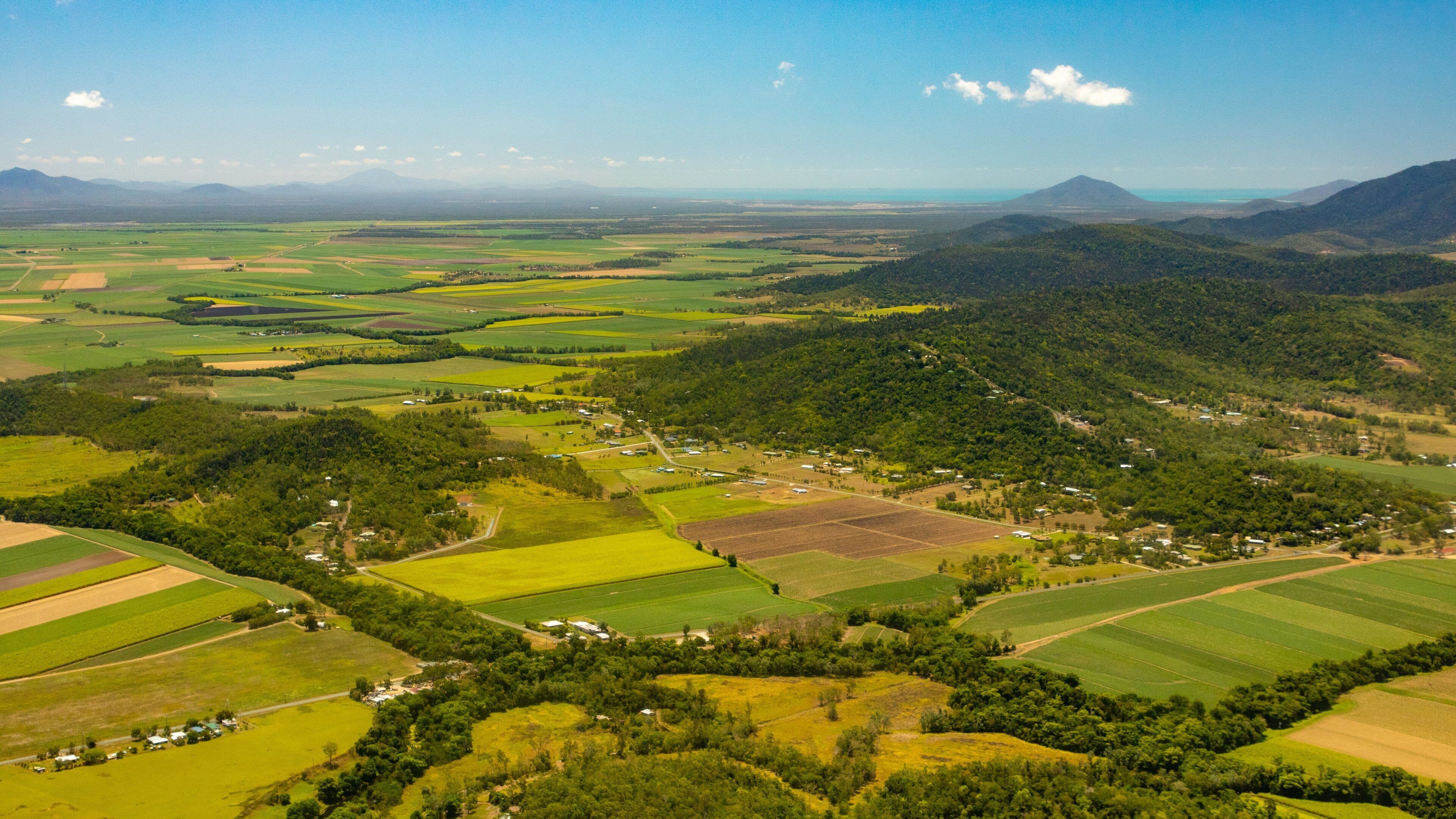 A rural landscape with fields, forests, and distant mountains.
