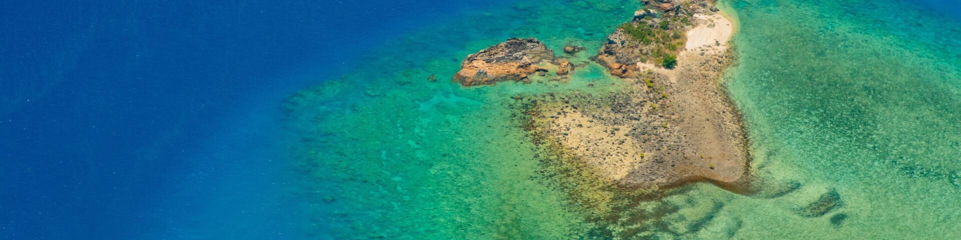 An aerial view of a small island with clear turquoise waters and a sandy beach.