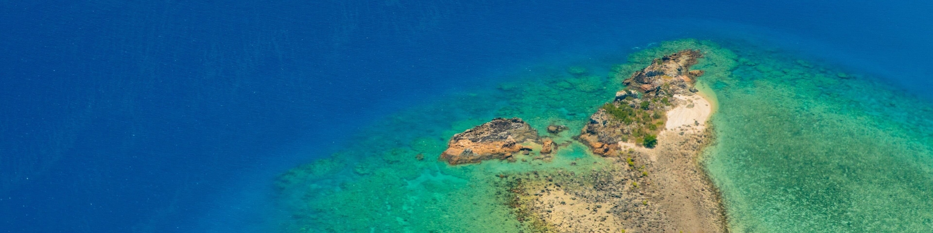 Vista aérea de una pequeña isla con aguas turquesas cristalinas y una playa de arena.