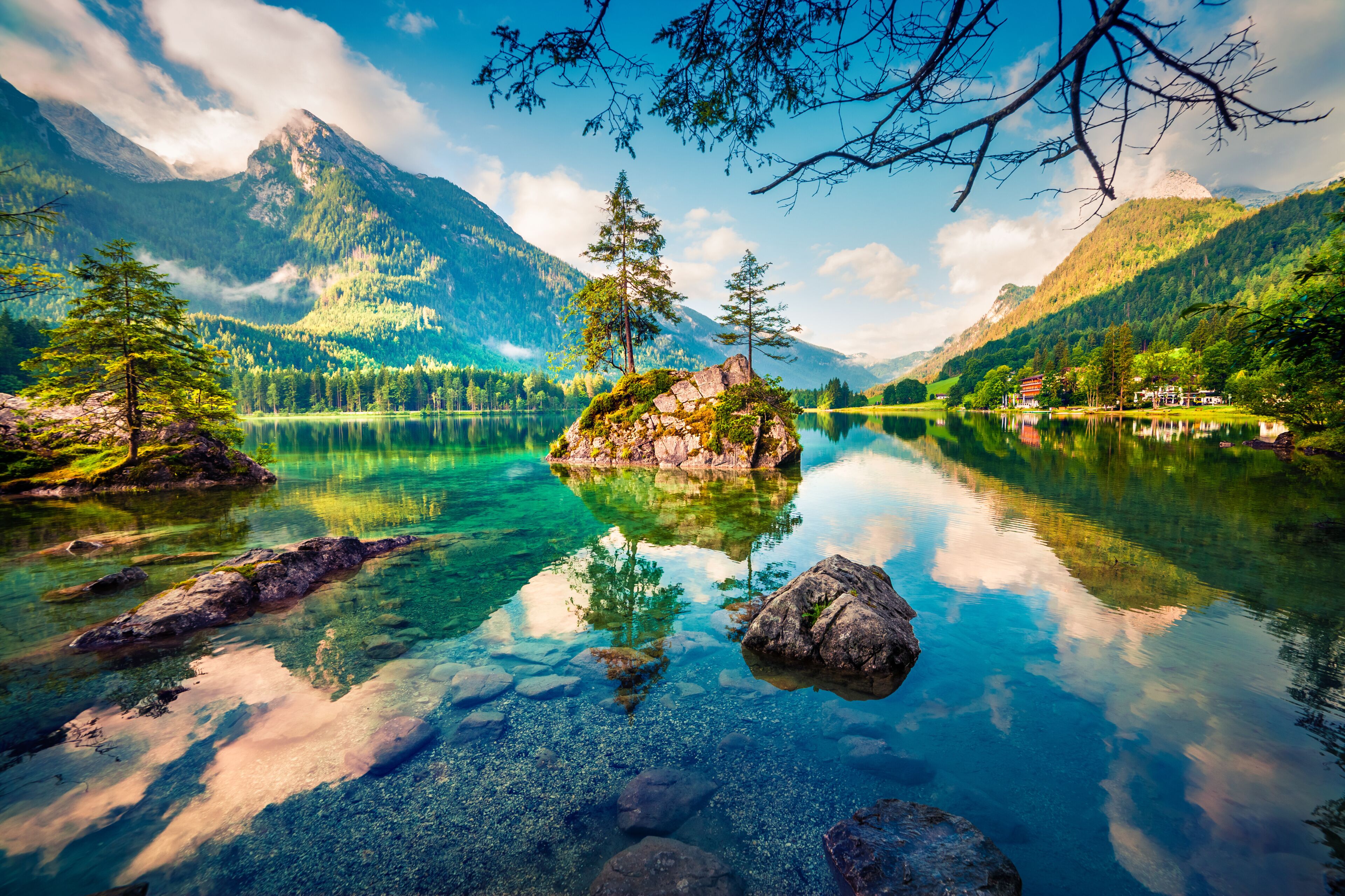 A mountain lake with clear water, surrounded by forested mountains and a small island with trees.