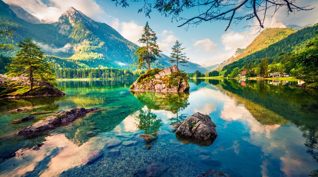 A mountain lake with clear water, surrounded by forested mountains and a small island with trees.