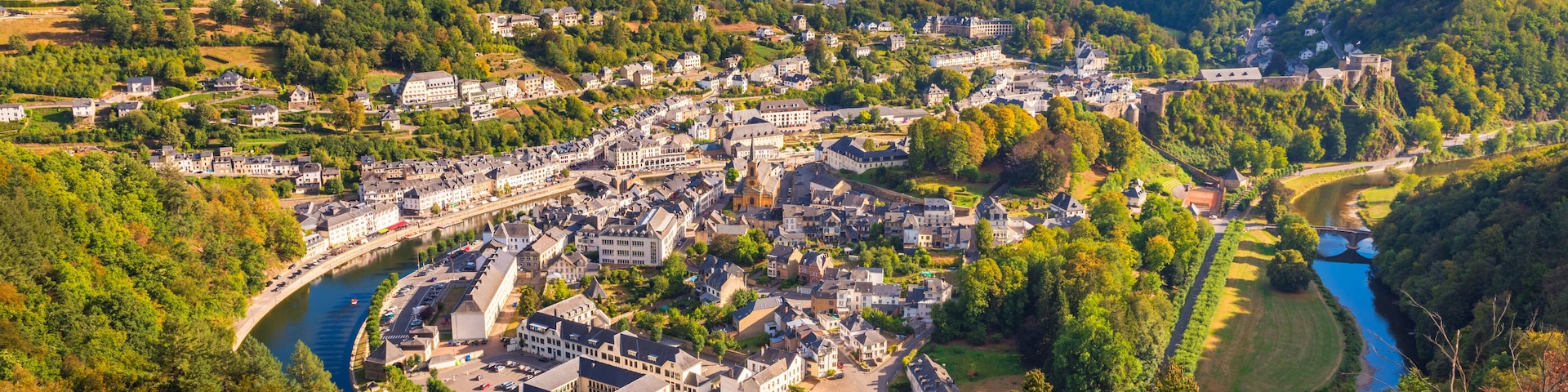 A town nestled in a valley with a river, surrounded by forested hills.
