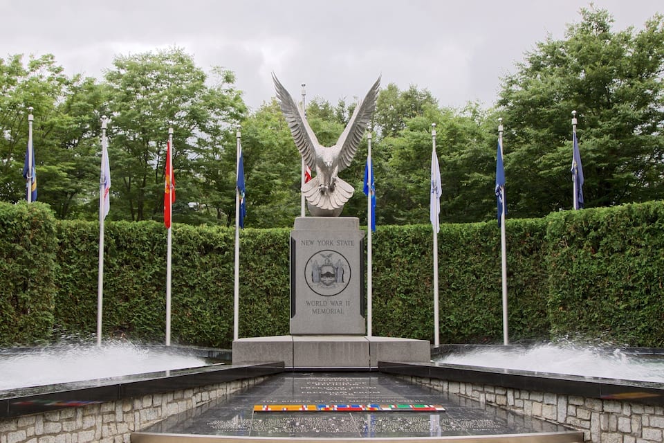 A memorial with a statue of an eagle, surrounded by flags and water features.