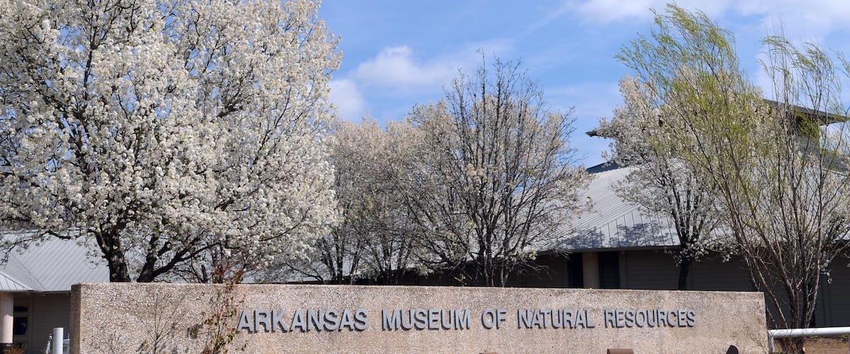 The Arkansas Museum of Natural Resources sign with blooming trees in the background.