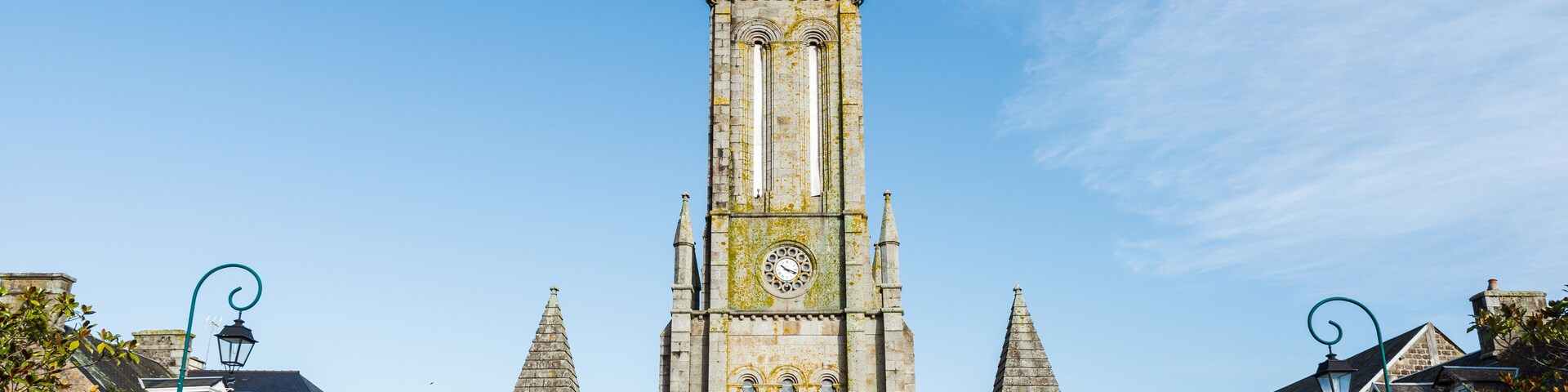 Eine historische Kirche mit einem hohen Turm, einer Uhr und einer Statue davor.