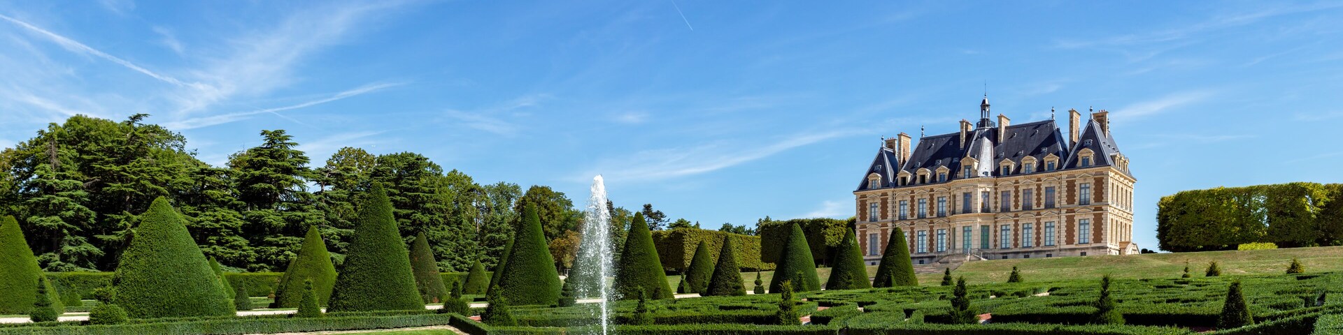 A grand château with a formal garden, including a circular pond and topiary trees.