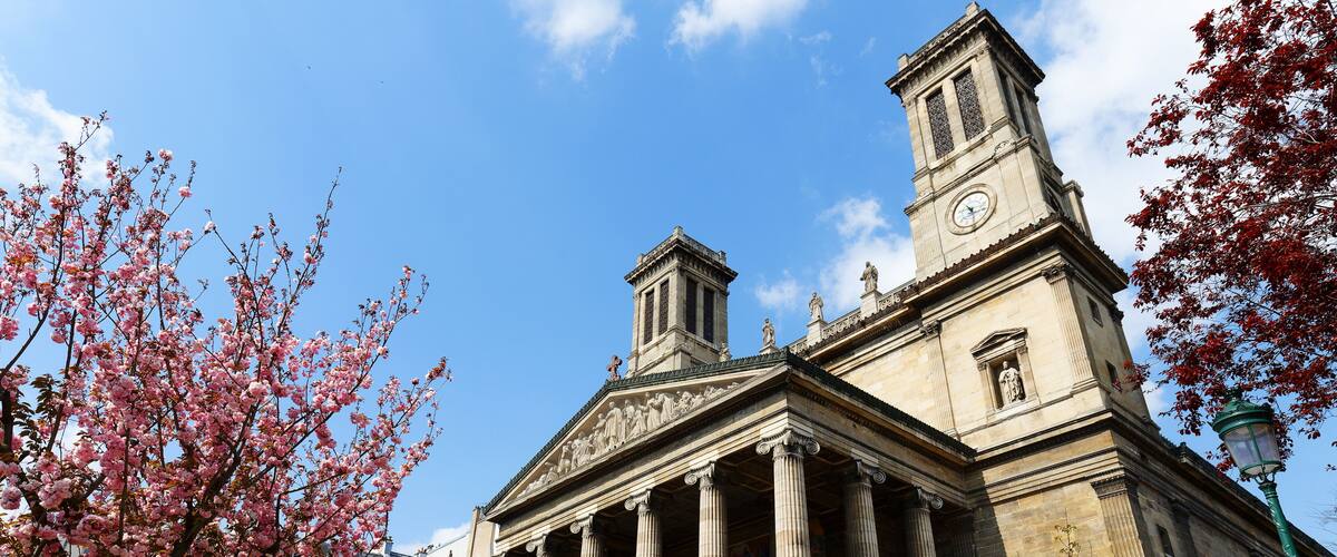 A classical building with columns, a clock tower, and a statue.