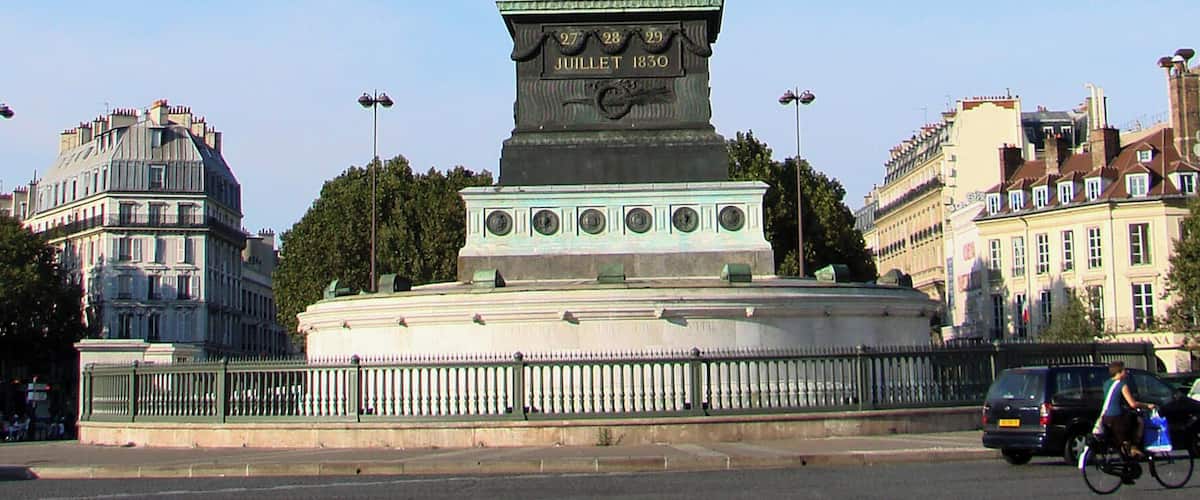 A tall, ornate monument with a statue on top, surrounded by a fence and set against a clear blue sky.