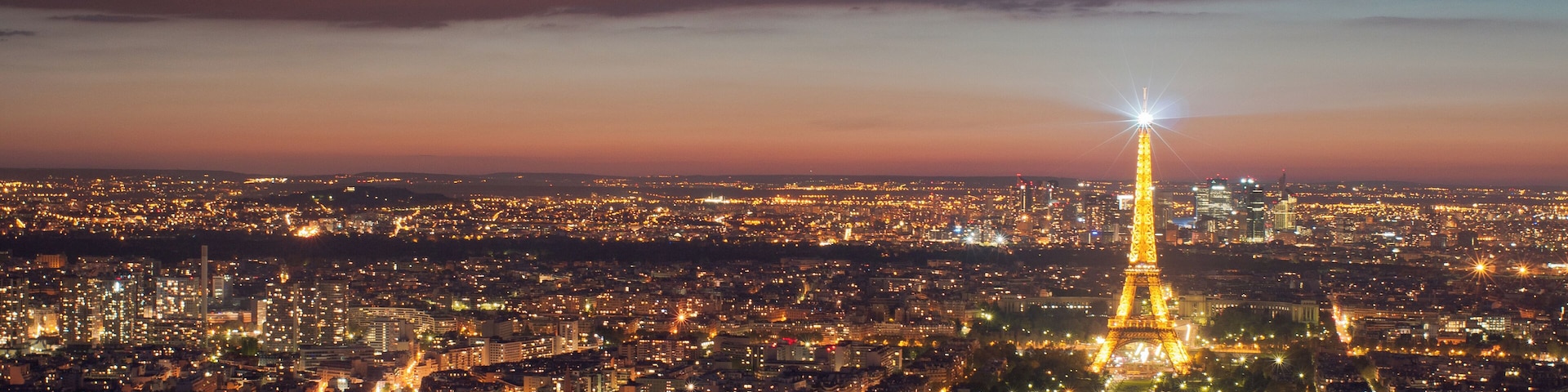 Un paisaje urbano nocturno con la Torre Eiffel iluminada, rodeada de edificios densos y un río.
