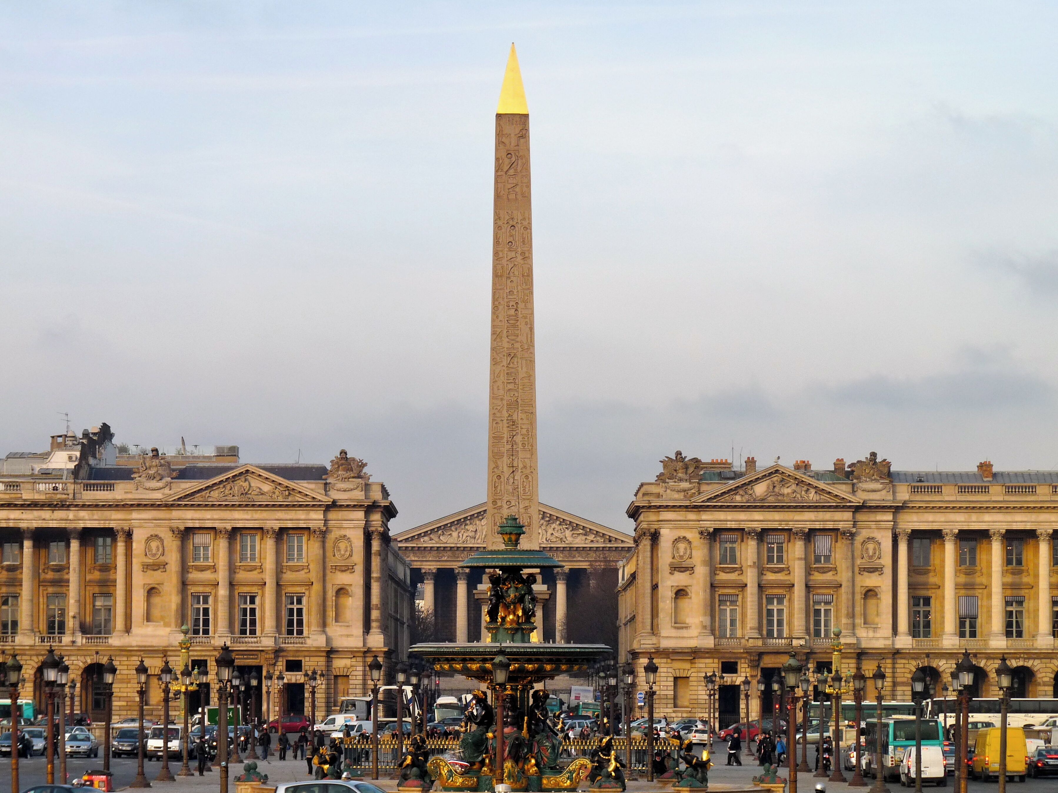 Un gran obelisco frente a un edificio clásico con columnas y una fuente en el centro.