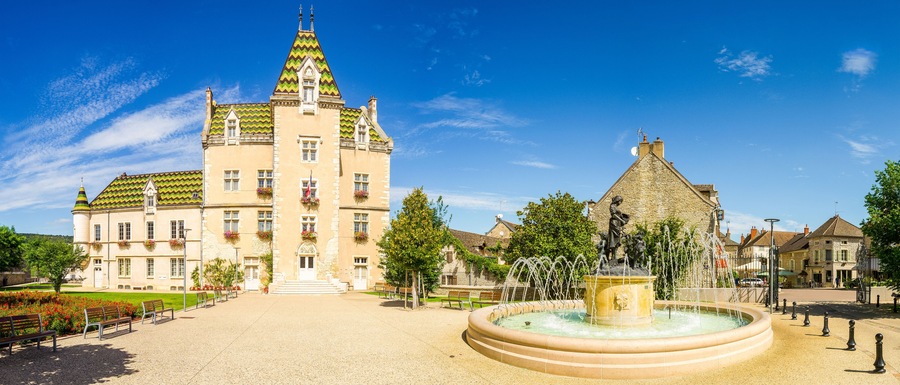 Un edificio histórico con una torre, una fuente y una estatua en una plaza pública.
