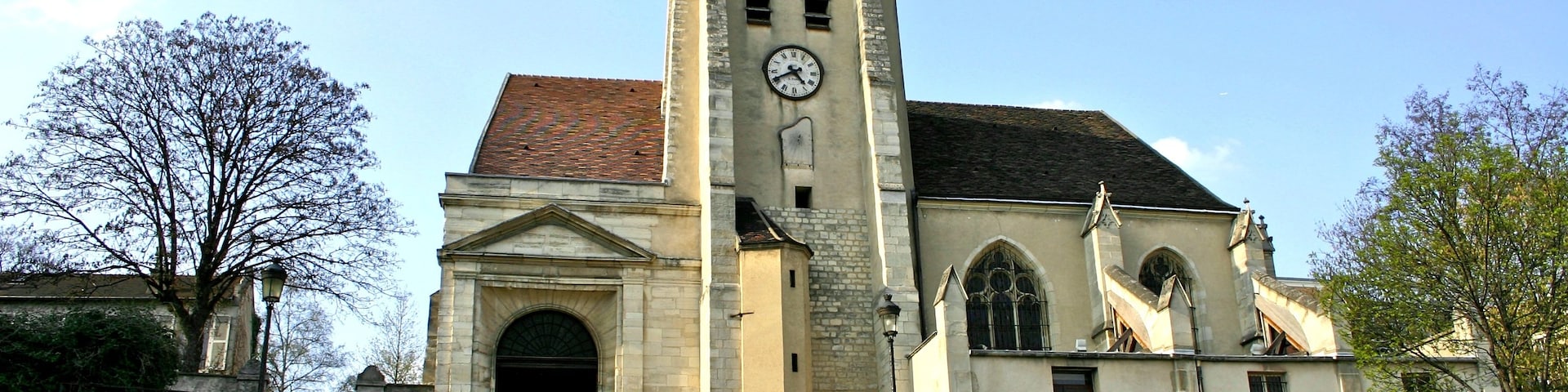 Una iglesia con una torre del reloj, escalones de piedra que conducen a la entrada y un cielo azul despejado.