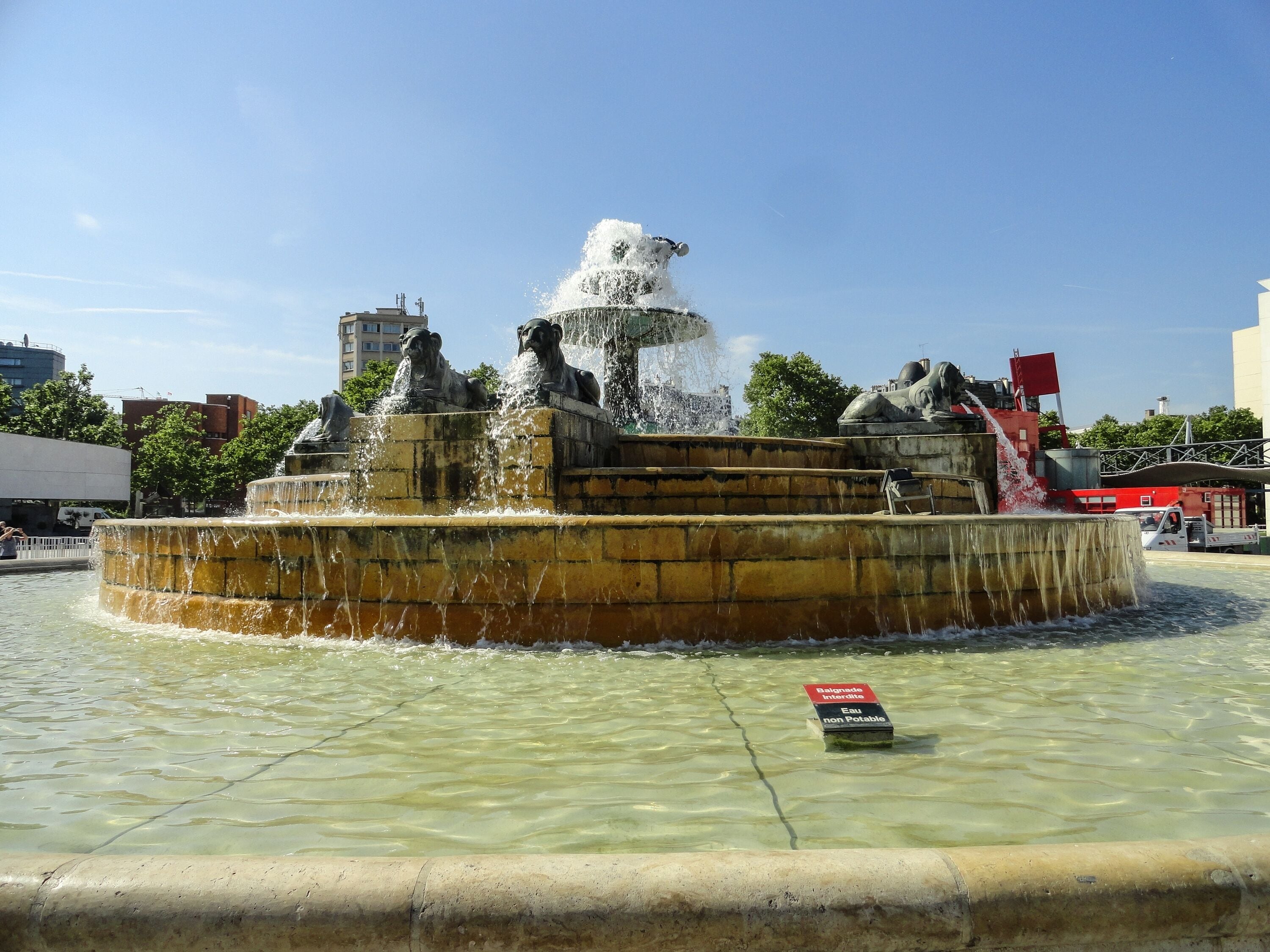 A fountain with statues and water jets, surrounded by a paved area.