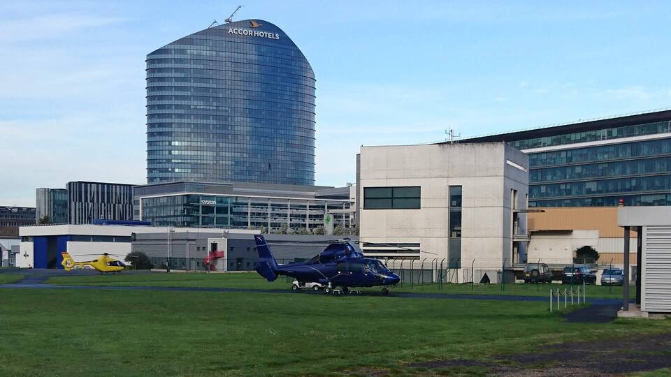 A helicopter on a grassy field, a modern building, and a tall skyscraper in the background.