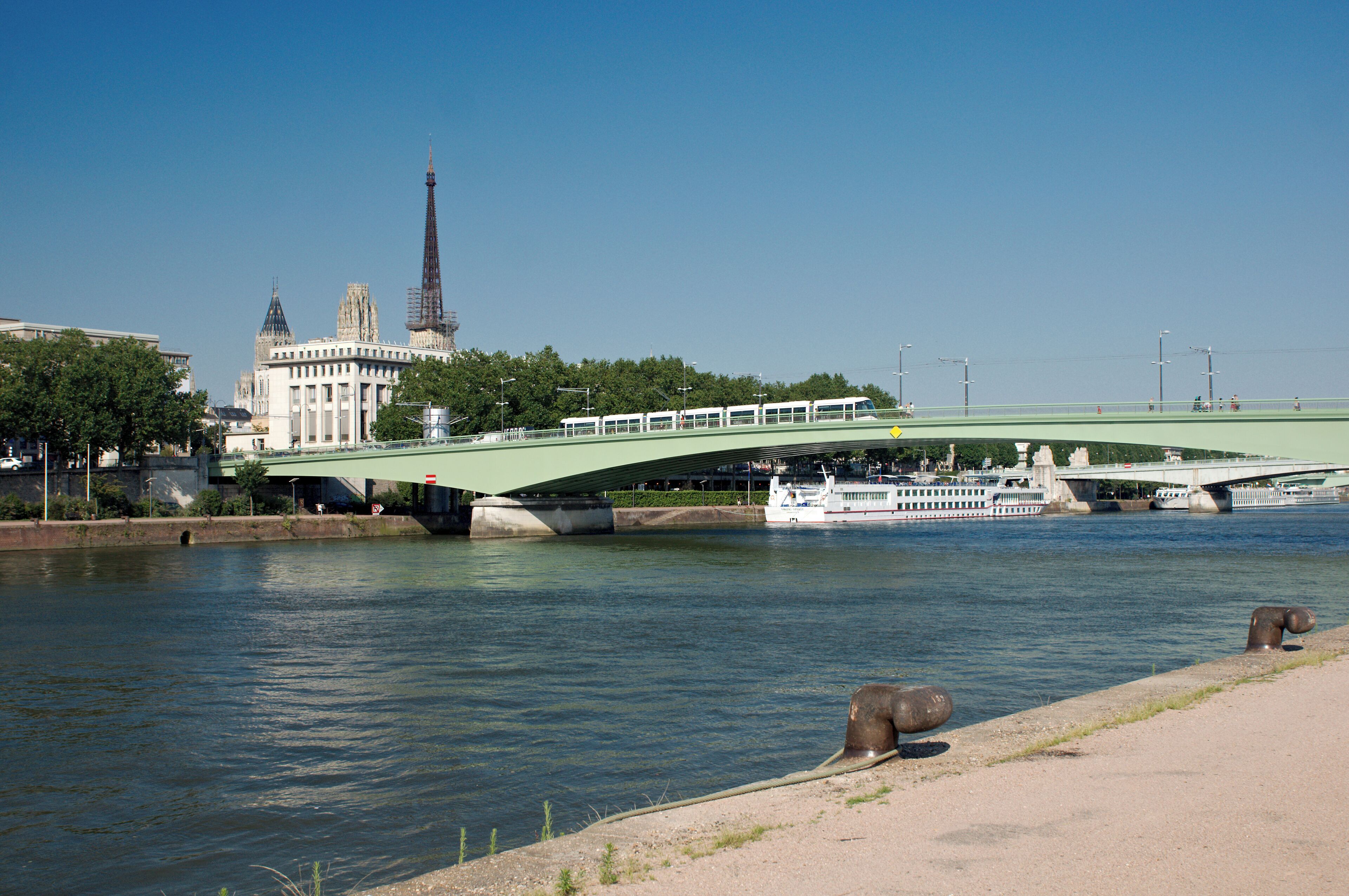 Le pont Jeanne-d’Arc enjambant la Seine à Rouen, avec une nouvelle rame de métro se déplaçant dessus et la cathédrale émergeant au-dessus des immeubles.