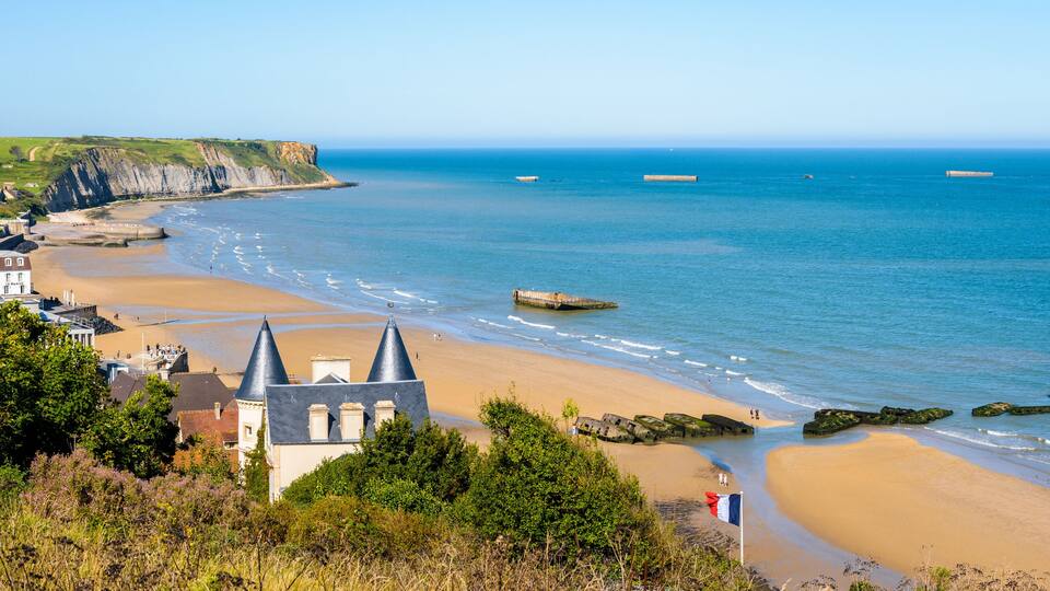 Panoramic view over Arromanches beach and Cap Manvieux in Normandy, France, on a sunny day, with remains of the WWII artificial Mulberry harbor lying on the sand and in the sea.