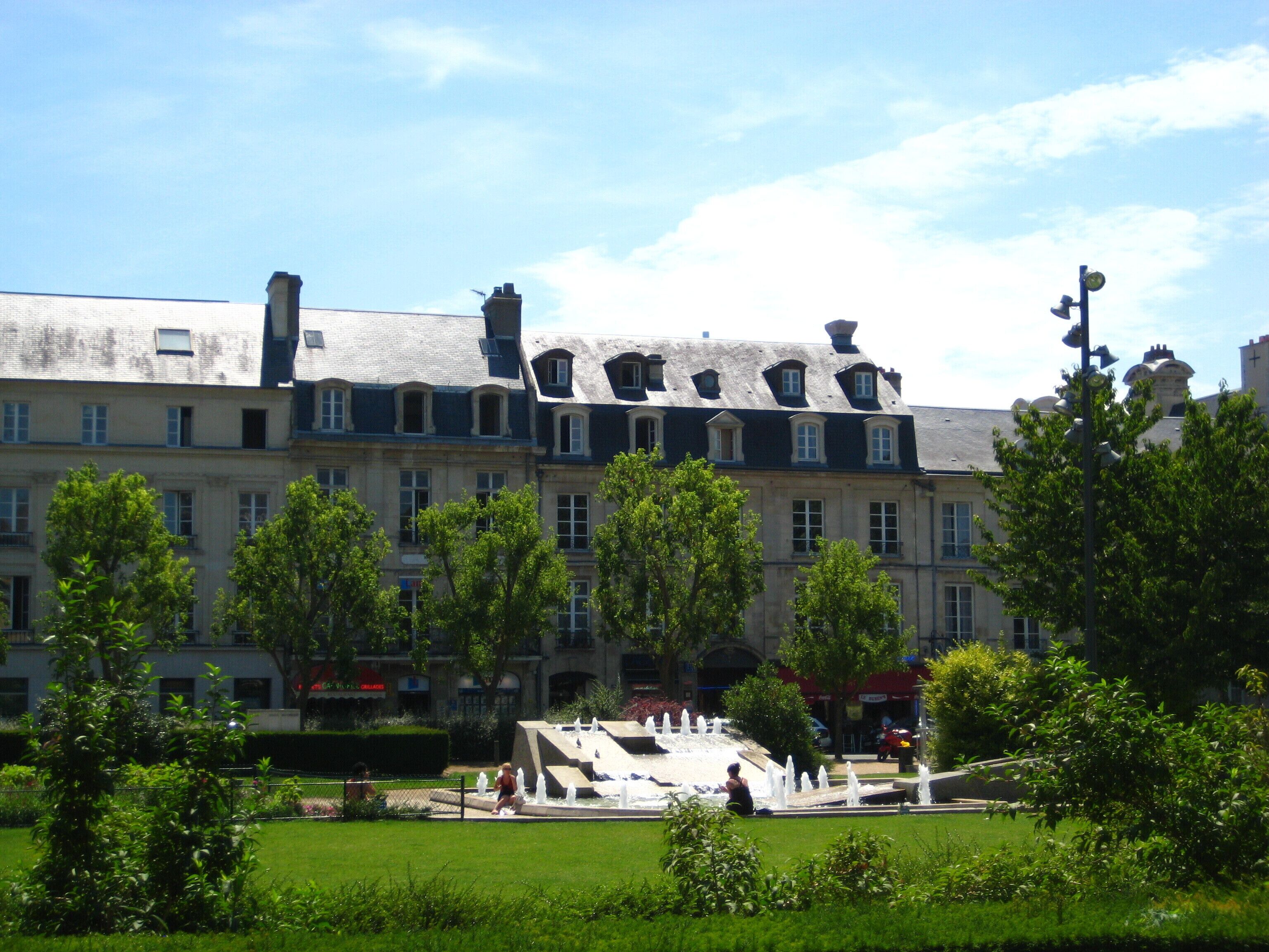 A historic building with multiple chimneys and a fountain in a park.