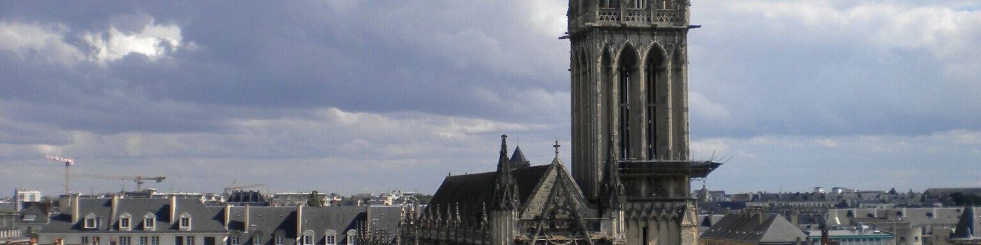 A historic cathedral with a tall spire, surrounded by urban buildings and a busy street.