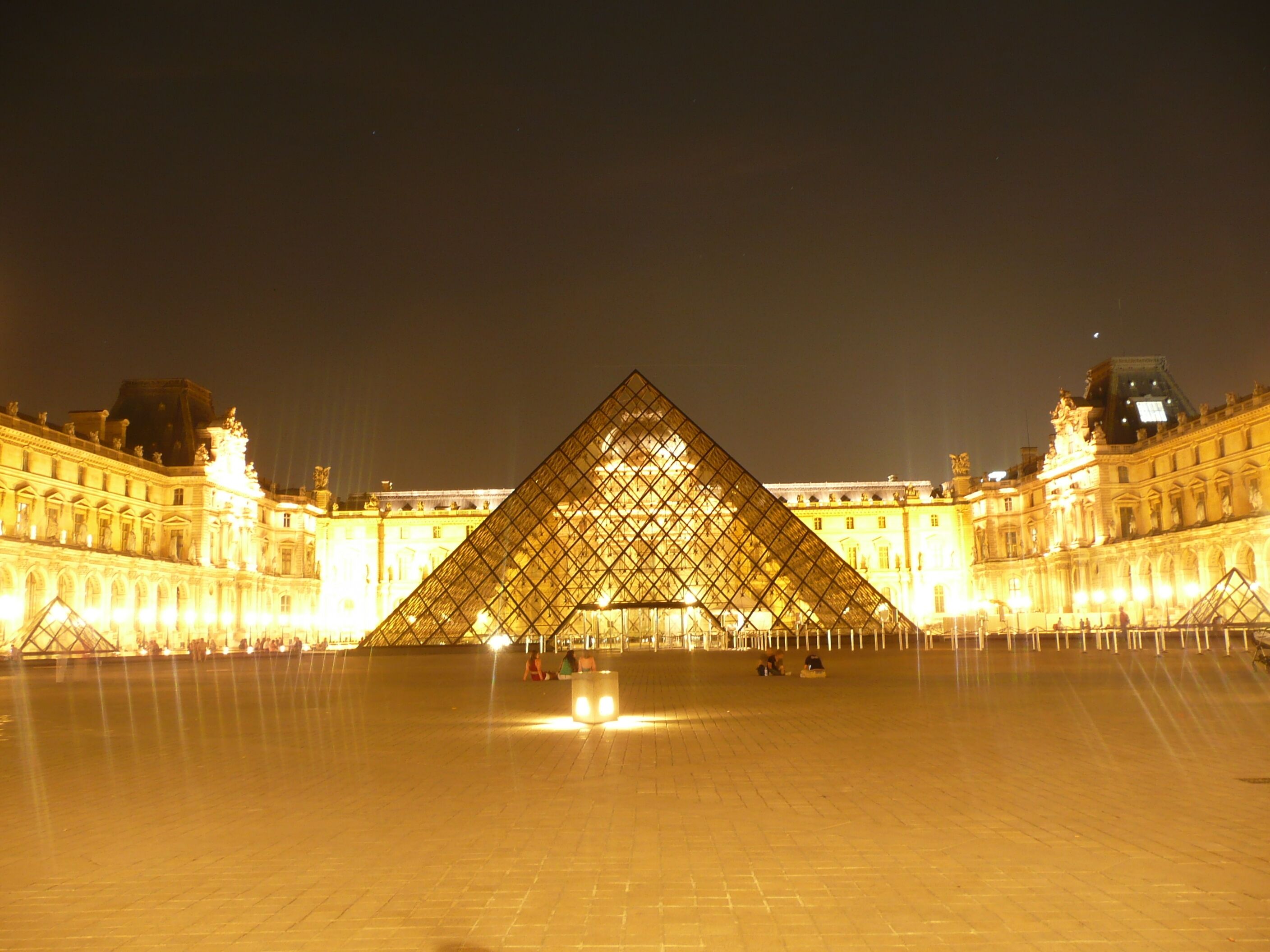 The Louvre Pyramid at night with the surrounding Louvre Museum buildings illuminated.
