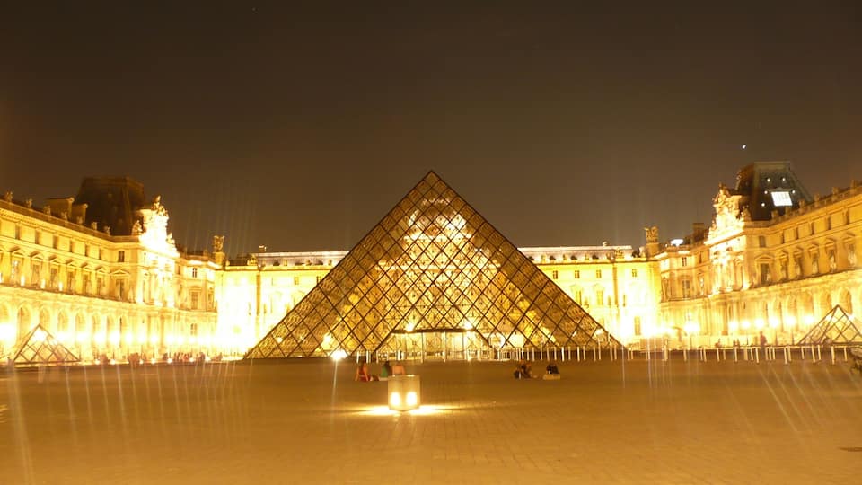 De Louvre Piramide 's nachts, met de omliggende verlichte gebouwen van het Louvre Museum.