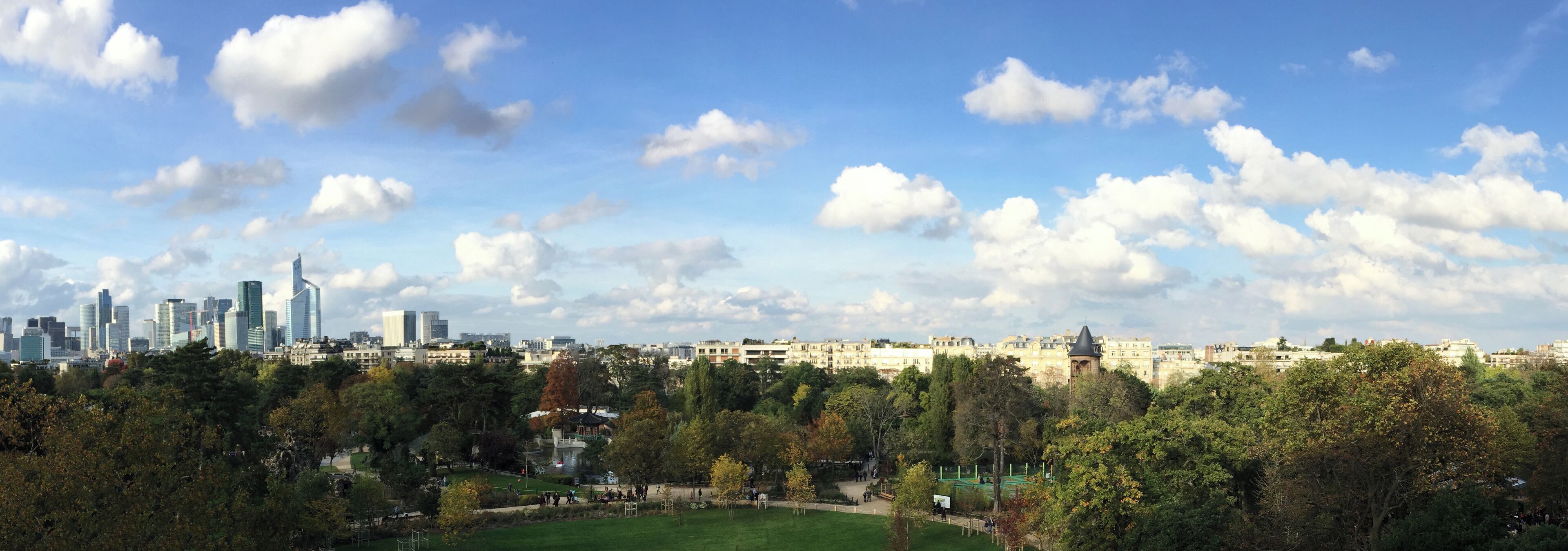 A city skyline with modern skyscrapers and a park with trees and a pond.
