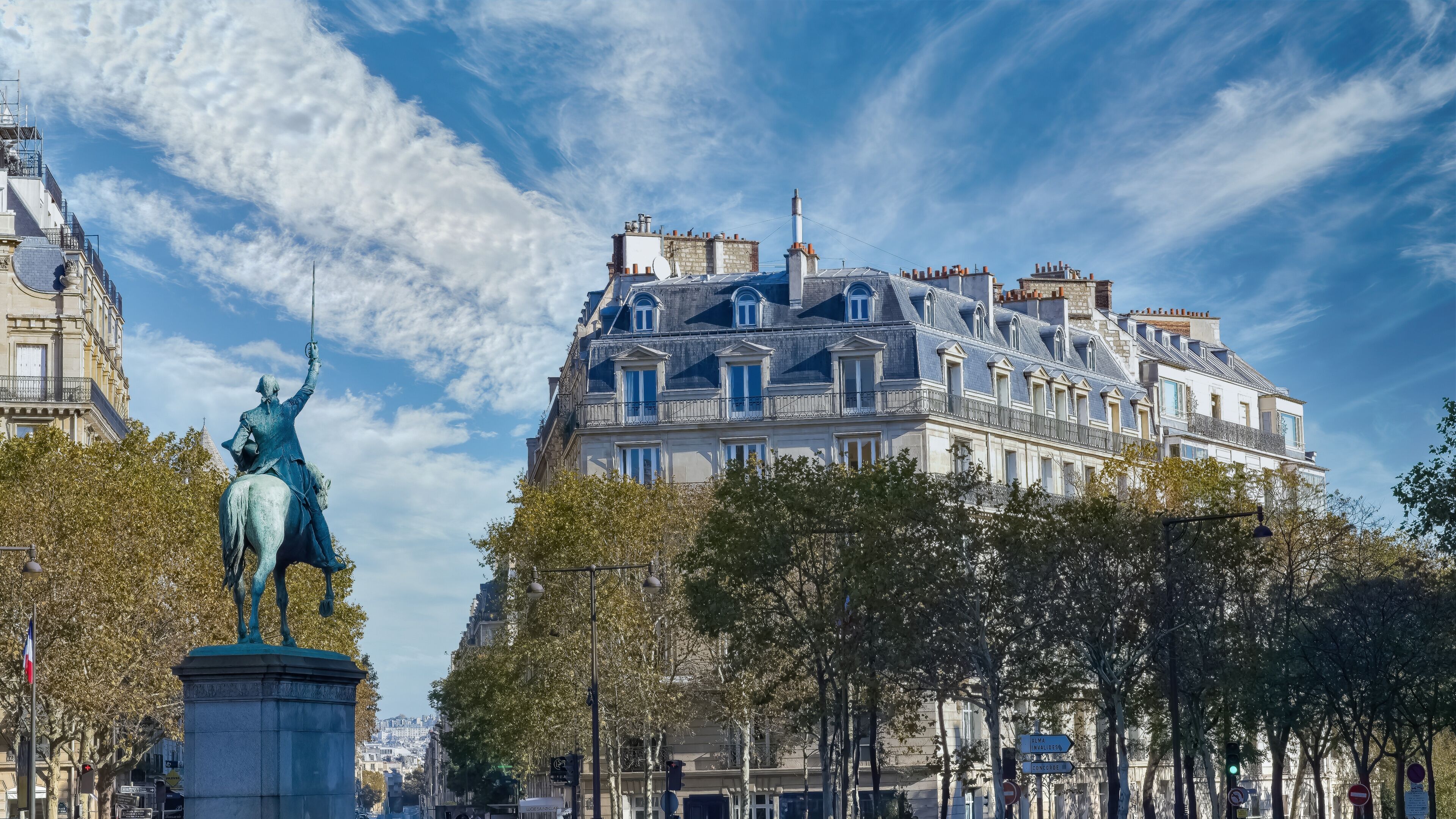 A statue of a historical figure on horseback, surrounded by trees and classic European architecture.
