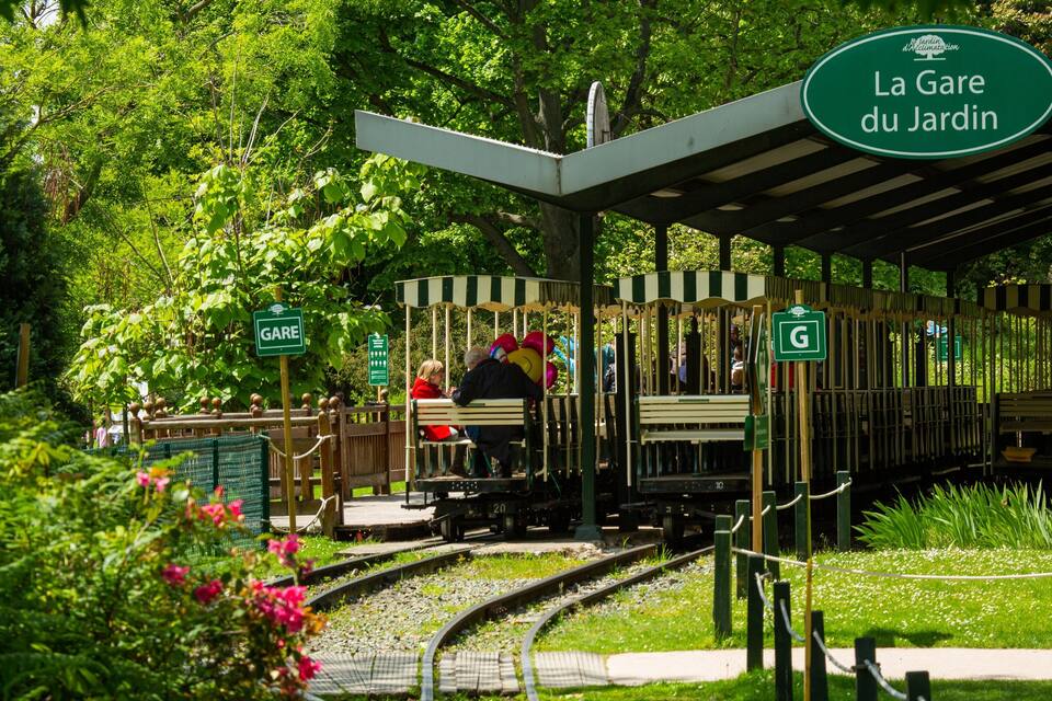 Un parco a tema giardino con una piccola ferrovia, panchine e vegetazione lussureggiante.