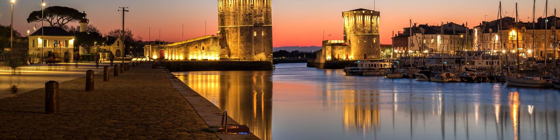 A historic waterfront at dusk with illuminated towers and a calm river reflecting the lights.