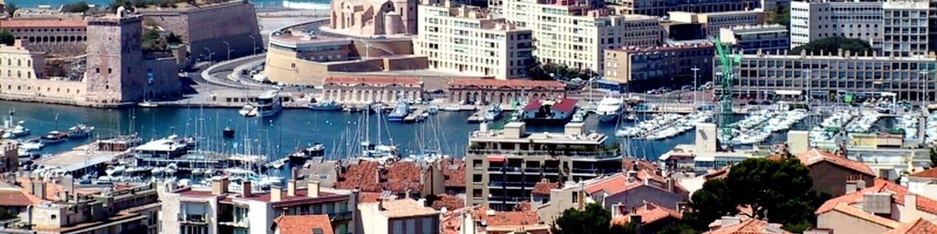 A coastal city with a marina, historic buildings, and a distant mountain range.