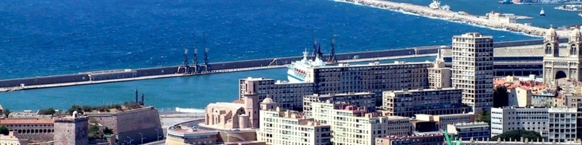 Uma cidade costeira com um porto de iates, edifícios históricos e uma cordilheira ao longe.