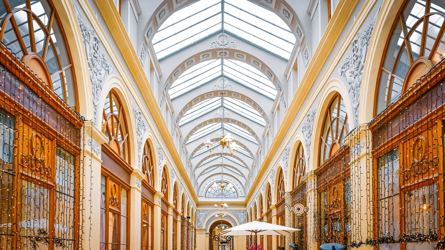 An ornate interior with a high arched ceiling, intricate wall carvings, and a central chandelier.