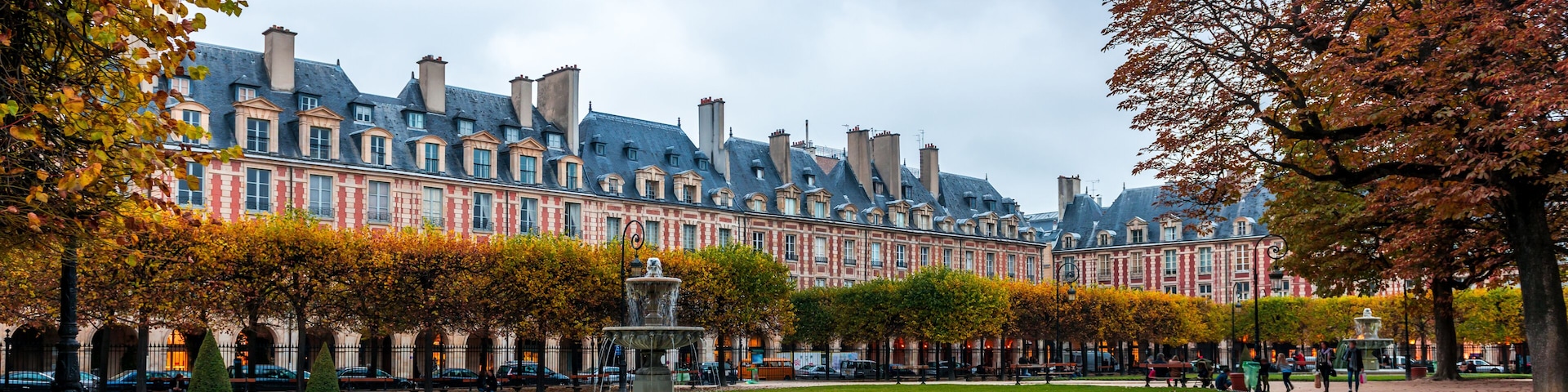 Un bĂątiment historique aux façades rouge et blanche, une fontaine centrale et un parc bien entretenu, agrĂ©mentĂ© dâarbres et dâune pelouse.