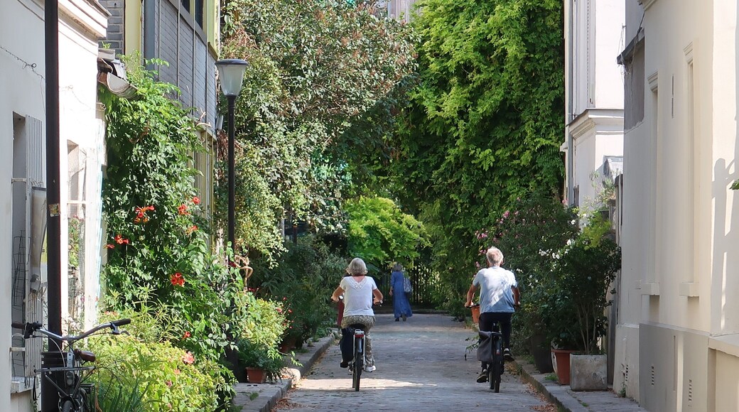 Cyclotourisme dans une ruelle végétalisée en ville, deux cyclistes séniors faisant du vélo en couple dans la verdoyante rue des Thermopyles à Paris, couverte de végétation (France)