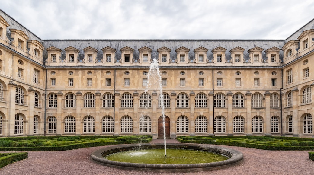 A historic building with a central fountain, symmetrical windows, and manicured hedges.
