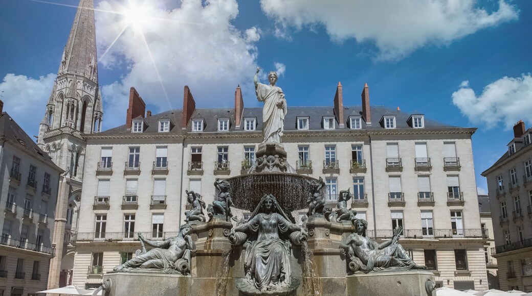 A historic building with a statue of a woman holding a child, a fountain with multiple statues, and a tall tower.