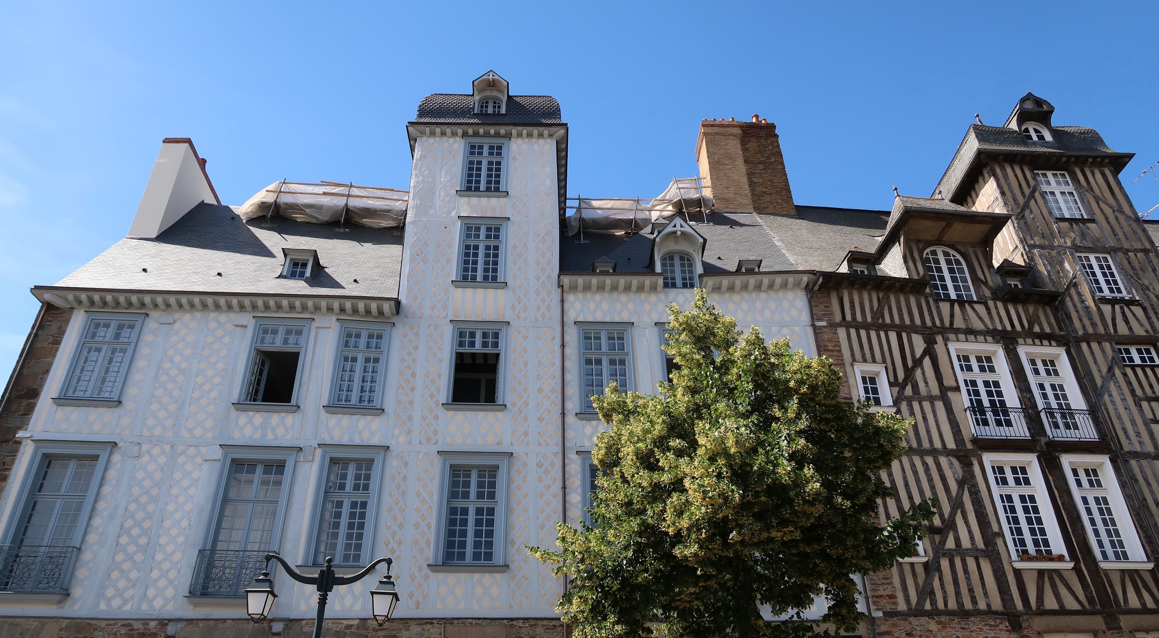 A historic building with a tower, multiple windows, and a tree in front.
